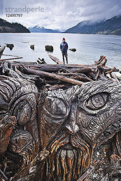 Eine Person steht hinter einigen Holzschnitzereien in der Nähe des Wassers in Squamish  British Columbia  Kanada.