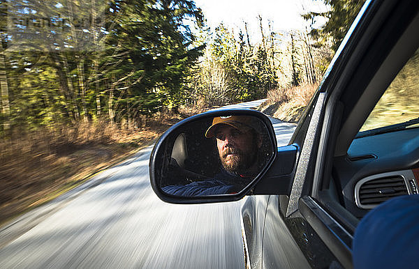 Das Gesicht eines Mannes spiegelt sich im Rückspiegel eines Lastwagens  während er eine Straße in Squamish  British Columbia  entlangfährt.