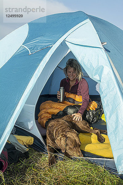 Eine Frau und ihr Chesapeake Bay Retriever Hund wachen in einem Zelt beim Camping auf Grassy Ridge auf