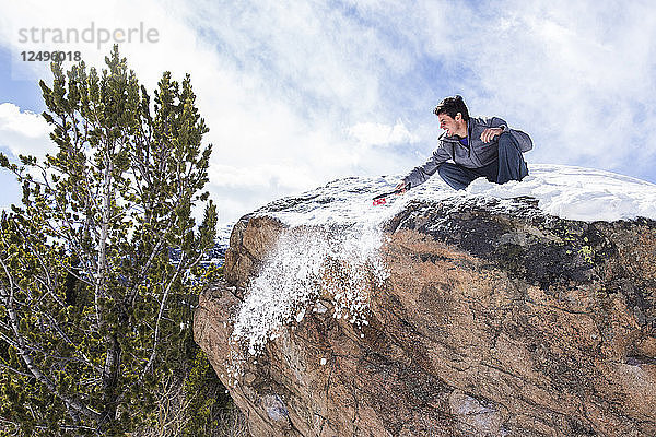 Männlicher Kletterer reinigt die Spitze eines Felsblocks vom Schnee  bevor er im Rocky Mountain National Park  Colorado  klettert.