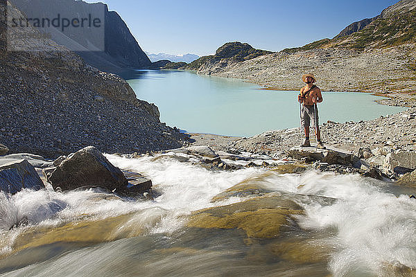 Ein Wanderer ohne Hemd steht am Ufer eines Flusses  der in den Wedgemount Lake im Garibaldi Provincial Park mündet.