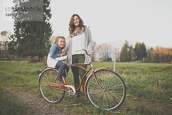Eine Mutter und ihre Tochter posieren mit einem altmodischen Fahrrad.
