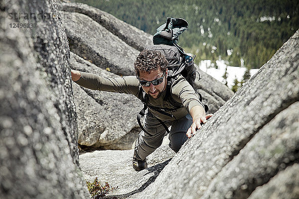 Ein Rucksacktourist klettert über Grantie-Felsen  um den Gipfelgrat des Needle Peak zu erreichen.