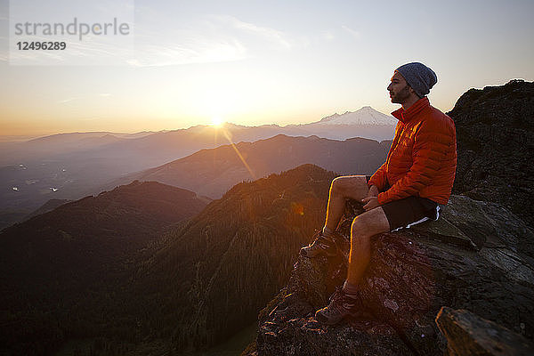 Ein Wanderer beobachtet den Sonnenuntergang von einer Felswand auf dem Gipfel des Sauk Mountain  Washington.