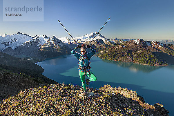 Eine Rucksacktouristin macht eine lustige Pose mit ihren Stöcken auf dem Gipfel des Panorama Ridge im Garibaldi Provincial Park  British Columbia  Kanada.