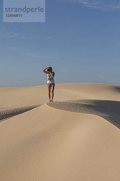 Mädchen (20 - 30 Jahre alt) in kurzen Hosen beim Fotografieren am Rande einer großen Sanddüne. Fuerteventura  Kanarische Inseln