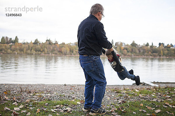 Ein Opa schwingt seine Enkelin in der Luft am Fluss