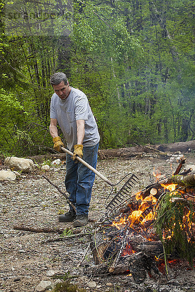 Ein Mann mittleren Alters kümmert sich bei der Gartenarbeit um ein großes Feuer.