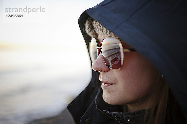 Porträt einer jungen Frau mit Sonnenbrille und Kapuzenjacke am White Rock Beach  British Columbia  Kanada.