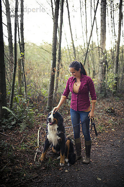 Porträt einer jungen Frau  die sich mit ihrem Berner Sennenhund in der freien Natur vergnügt.