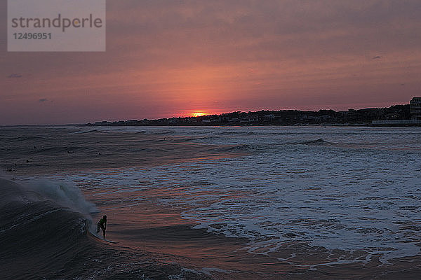 Ein Surfer fängt eine Welle  während die Sonne untergeht.