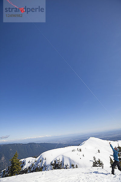Mann fliegt einen Drachen auf dem Gipfel eines schneebedeckten Berges