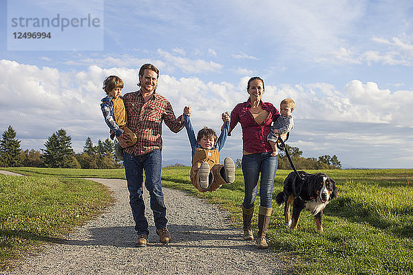 Eine fünfköpfige Familie mit Hund spaziert spielerisch über einen Kiesweg in einem örtlichen Park in der Nähe von Vancouver  Kanada.