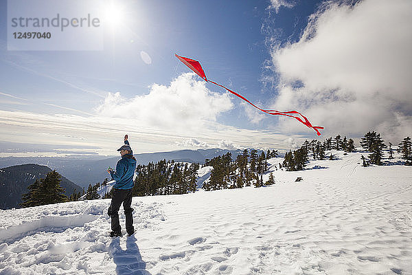 Ein Wanderer fliegt einen Drachen auf dem Gipfel eines schneebedeckten Berges