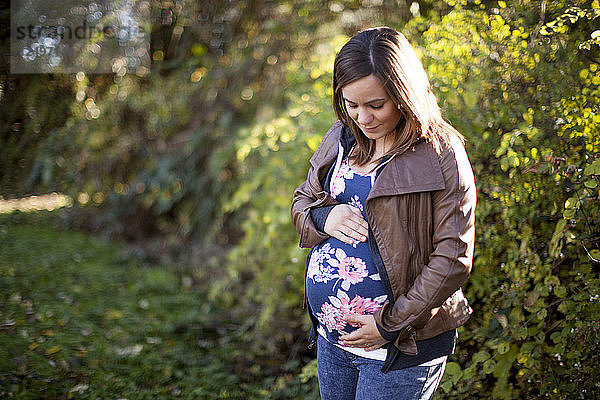 Outdoor-Porträt einer schönen jungen schwangeren Frau  die ihren Babybauch hält.