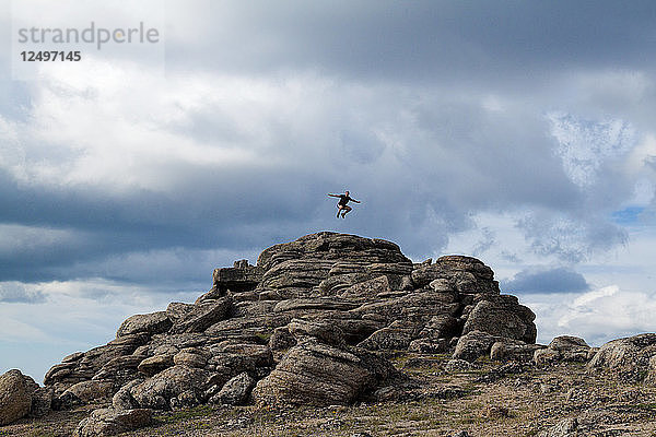Ein Rucksacktourist springt von einer Felsformation in Cliff City  einem Gebiet mit einzigartiger Geologie im Cathedral Lakes Provincial Park  British Columbia  Kanada  in die Luft.