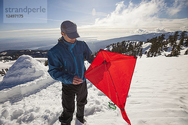 Ein Wanderer  der sich darauf vorbereitet  einen Drachen auf dem Gipfel eines schneebedeckten Berges steigen zu lassen