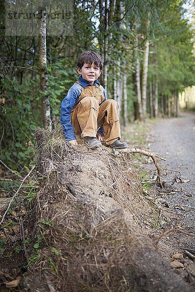 Porträt eines kleinen Jungen  der draußen auf einem Haufen Erde sitzt.