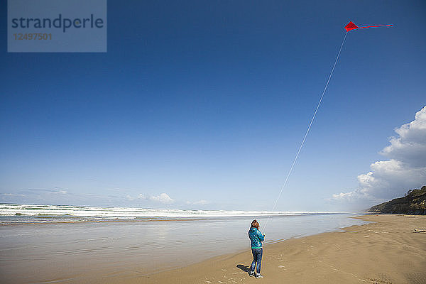 Eine junge Frau lässt einen roten Drachen in den Himmel steigen  während sie einen Strand an der Küste von Oregon besucht