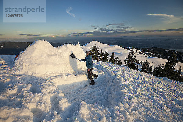 Ein Mann benutzt eine Schaufel  um sein Iglu auf dem Seymour Mountain  Kanada  fertig zu stellen