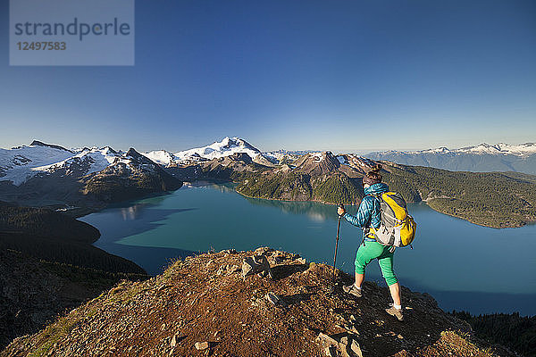 Ein Rucksacktourist erreicht den Gipfel des Panorama Ridge mit Blick auf den Garibaldi Lake im Garibaldi Provincial Park  British Columbia  Kanada.