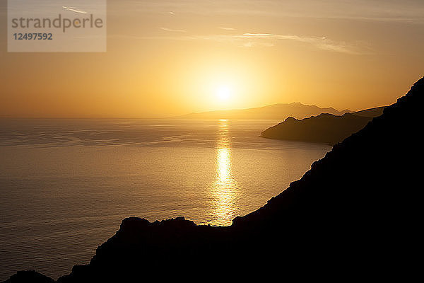 Goldener Sonnenuntergang auf einem sehr ruhigen Meer mit einer Klippensilhouette