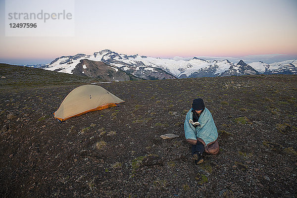 Eine junge Frau liest ein Buch beim Zelten auf der Panorama Ridge im Garibaldi Provincial Park  British Columbia  Kanada.