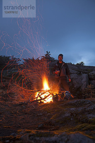 Porträt eines Bergsteigers  der sich neben einem alpinen Lagerfeuer warm hält