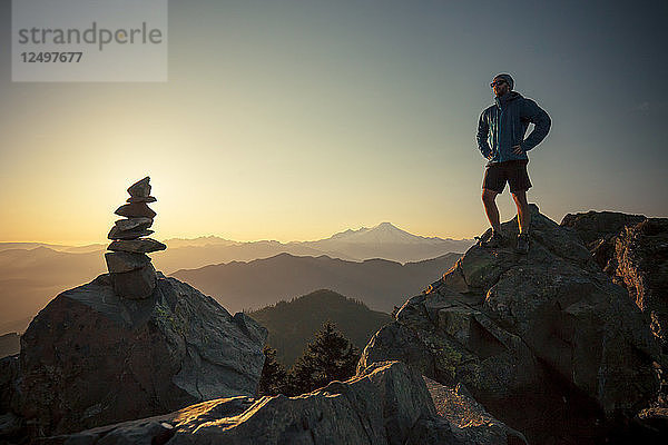 Ein Wanderer steht auf einem großen Felsen gegenüber dem Gipfelstein des Sauk Mountain in der North Cascade Mountain Range  Washington.