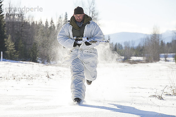Ein Jäger in einem Tarnanzug für kaltes Wetter trägt sein Gewehr  während er durch ein schneebedecktes Feld in British Columbia  Kanada  läuft.