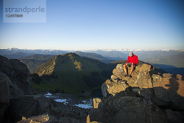 Ein Mann arbeitet an einem Tablet  während er auf dem Gipfel des Sauk Mountain in Washington sitzt.