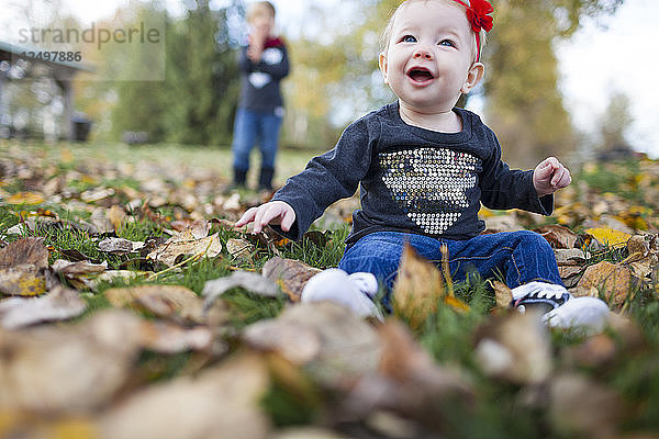 Ein lächelndes Baby  das mit Blättern im Park spielt