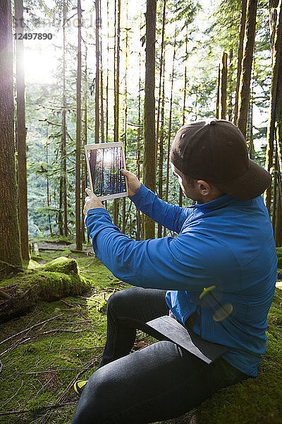 Ein Mann fotografiert mit einem Tablet die Morgensonne  die durch den Wald scheint.