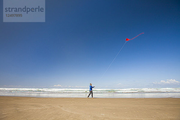 Ein junger Mann lässt bei einem Strandspaziergang an der Küste von Oregon einen roten Drachen in den Himmel steigen