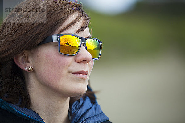 Haystack Rock und Cannon Beach spiegeln sich in der bunten Sonnenbrille einer jungen Frau.