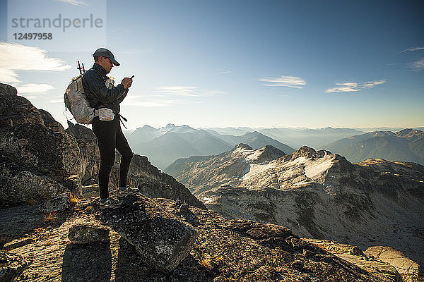 Ein Ultraleicht-Rucksacktourist sendet eine Sicherheitsnachricht von seinem Smartphone  während er hoch in den Bergen bei Whistler  BC  Kanada  wandert.