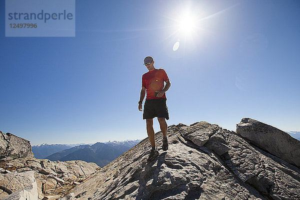 Ein Wanderer geht mit seinem Smartphone in der Hand auf dem Gipfel des Cassiope Peak in der Nähe von Pemberton  British Columbia  Kanada  entlang eines felsigen Grats.