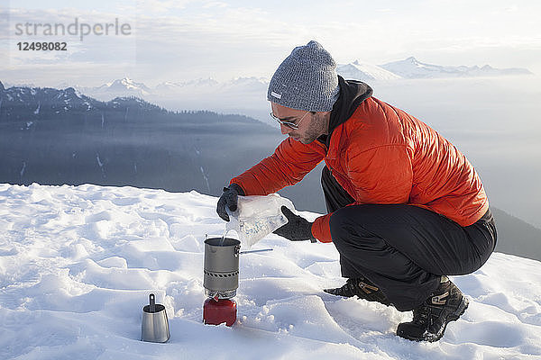 Ein Bergsteiger gießt Wasser in einen Campingkocher beim Zelten in den Bergen von British Columbia  Kanada.