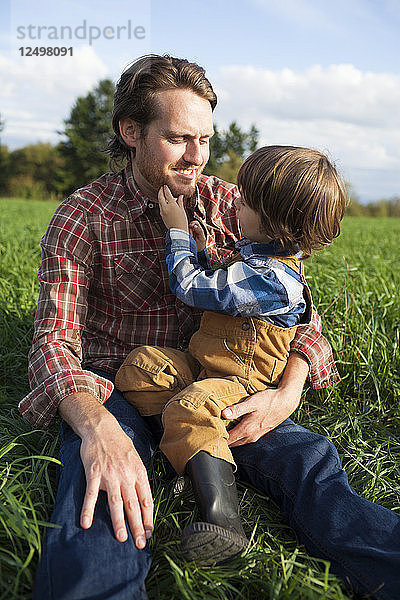 Ein Vater sitzt mit seinem kleinen Sohn zusammen  während der Sohn mit seinem Bart spielt.