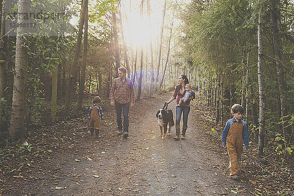 Eine fünfköpfige Familie mit einem Hund genießt einen Morgenspaziergang auf einem Kiesweg in einem örtlichen Park.