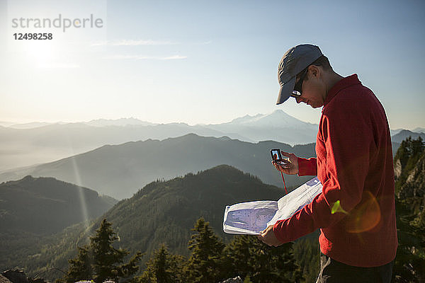 Ein Mann benutzt einen Kompass und eine Papierkarte  um bei einer Wanderung in der North Cascade Mountain Range zu navigieren.