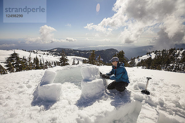 Ein Mann benutzt Schnee  um die Risse in den ersten beiden Reihen eines Block-Iglus auf dem Seymour Mountain  Kanada  zu füllen