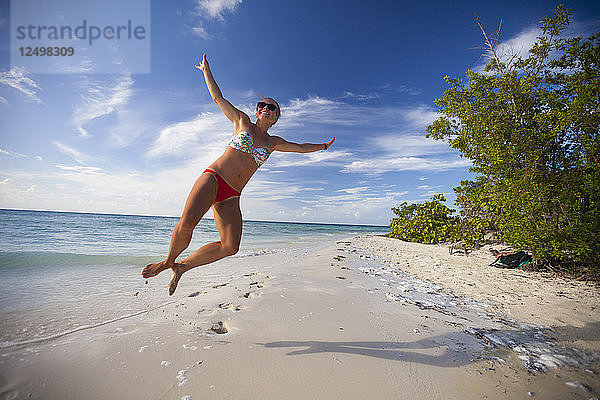 Ein junger attraktiver Mann springt in die Luft und macht am Strand von Cayo Coco  Kuba  einen Fersenklick.