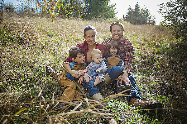 Ein lustiges Porträt einer lebhaften fünfköpfigen Familie  die auf einem Feld sitzt.