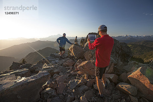 Ein Mann macht mit einem Tablet ein Foto von seinem Freund auf dem Gipfel des Sauk Mountain in Washingotn.