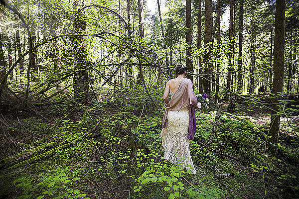 Eine Frau in einem Kleid hält einen Blumenstrauß in einer Waldlandschaft.