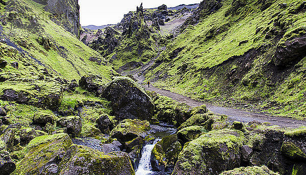 Langzeitbelichtung von Mann zu Fuß in einem grünen Canyon in Island
