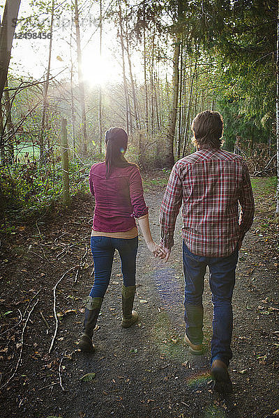 Ein junges Paar hält sich an den Händen  während es in einem örtlichen Park spazieren geht.