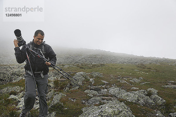 Mann mit der Kamera auf dem Gipfel des Mount Washington bei starker Bewölkung