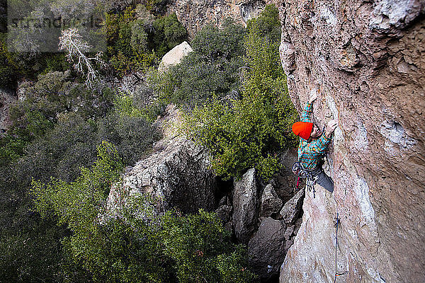 Ein männlicher Kletterer mit orangefarbener Mütze und mehrfarbigem Hemd klettert Family Jewel (5.10d) am Mount Gorgeous im Malibu Canyon State Park in Malibu  Kalifornien. Family Jewel ist eine sehr beliebte Sportkletterei im Malibu Canyon.